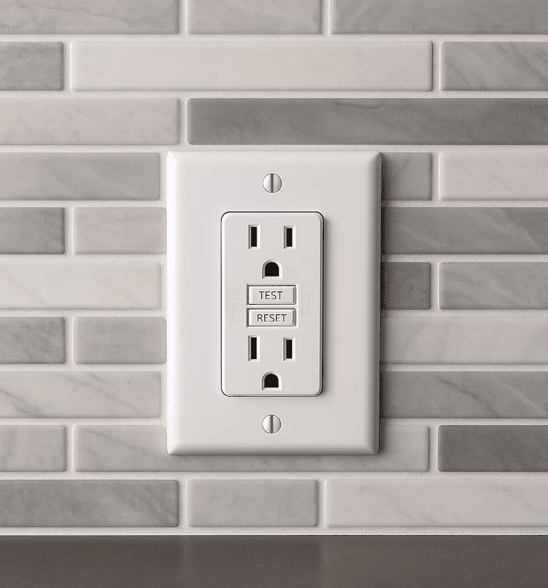 0c7aebf3-fdb4-4392-8f9d-380fbd3d6b6e A close-up of a modern kitchen backsplash with a GFCI outlet installed, showing a “Test” and “Reset” button.