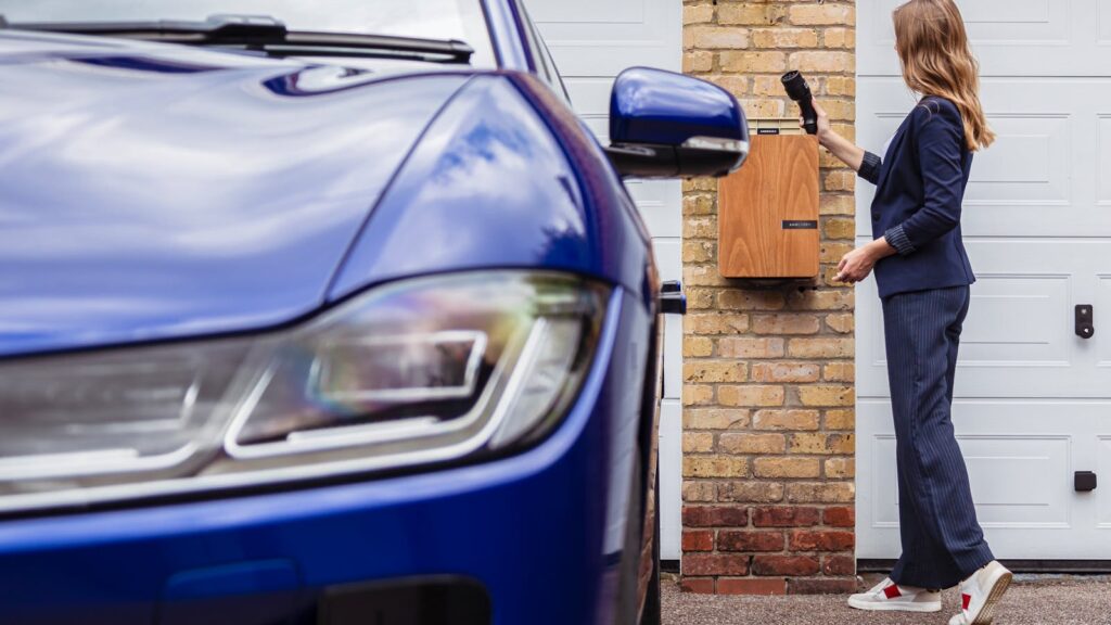 Woman charging an electric car at a home EV station, promoting charger rebates and incentives