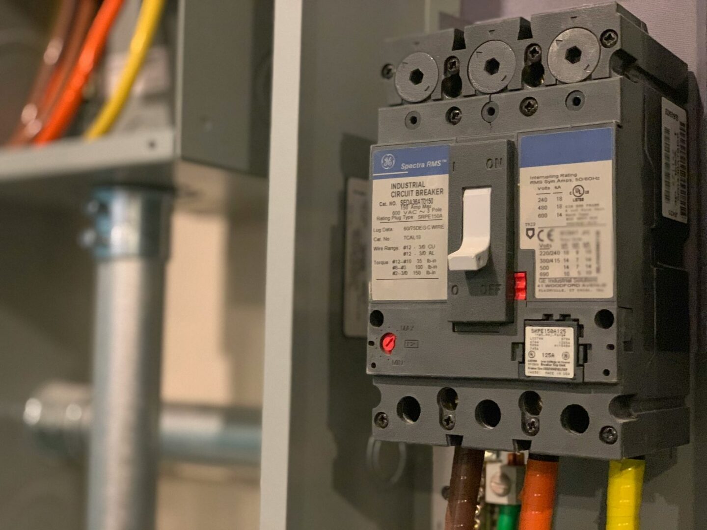 Close up of a gray GE Spectra RMS molded case circuit breaker with its handle in the off position mounted inside an enclosure.