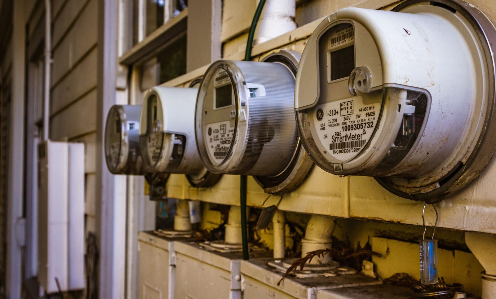 Three round GE smart electric meters mounted in sockets on the yellow clapboard siding of a house.