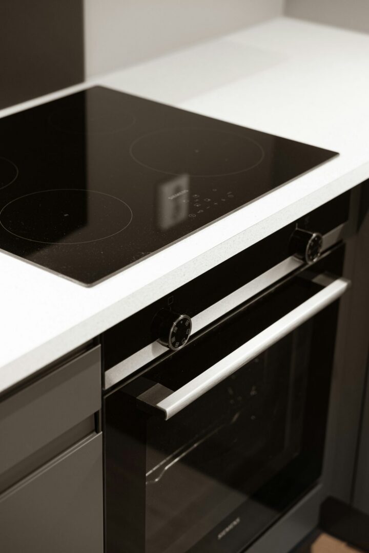 A black glass induction cooktop set into a white counter above a built in oven.