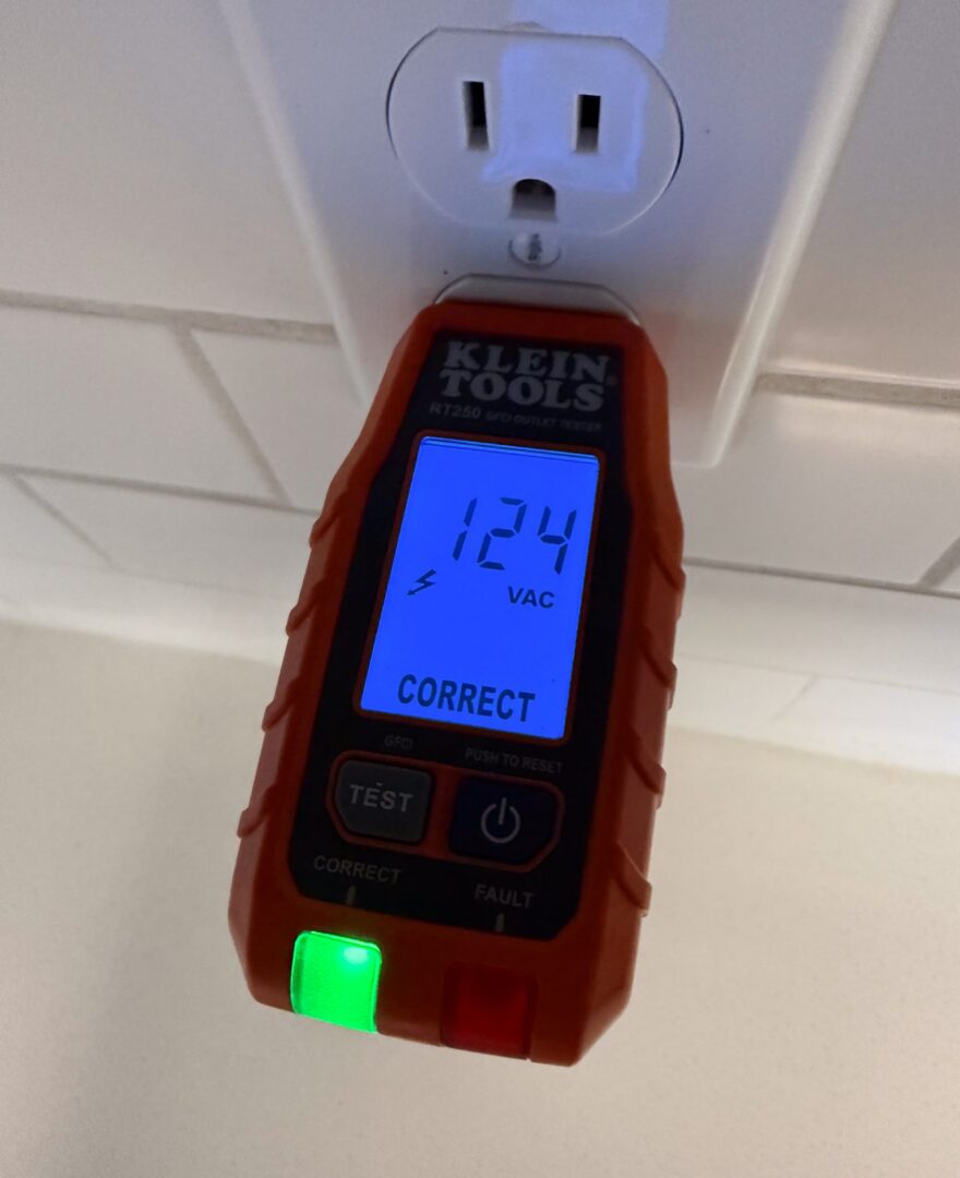 A Klein Tools digital receptacle tester plugged into a white outlet showing 124 VAC and CORRECT with a green light.