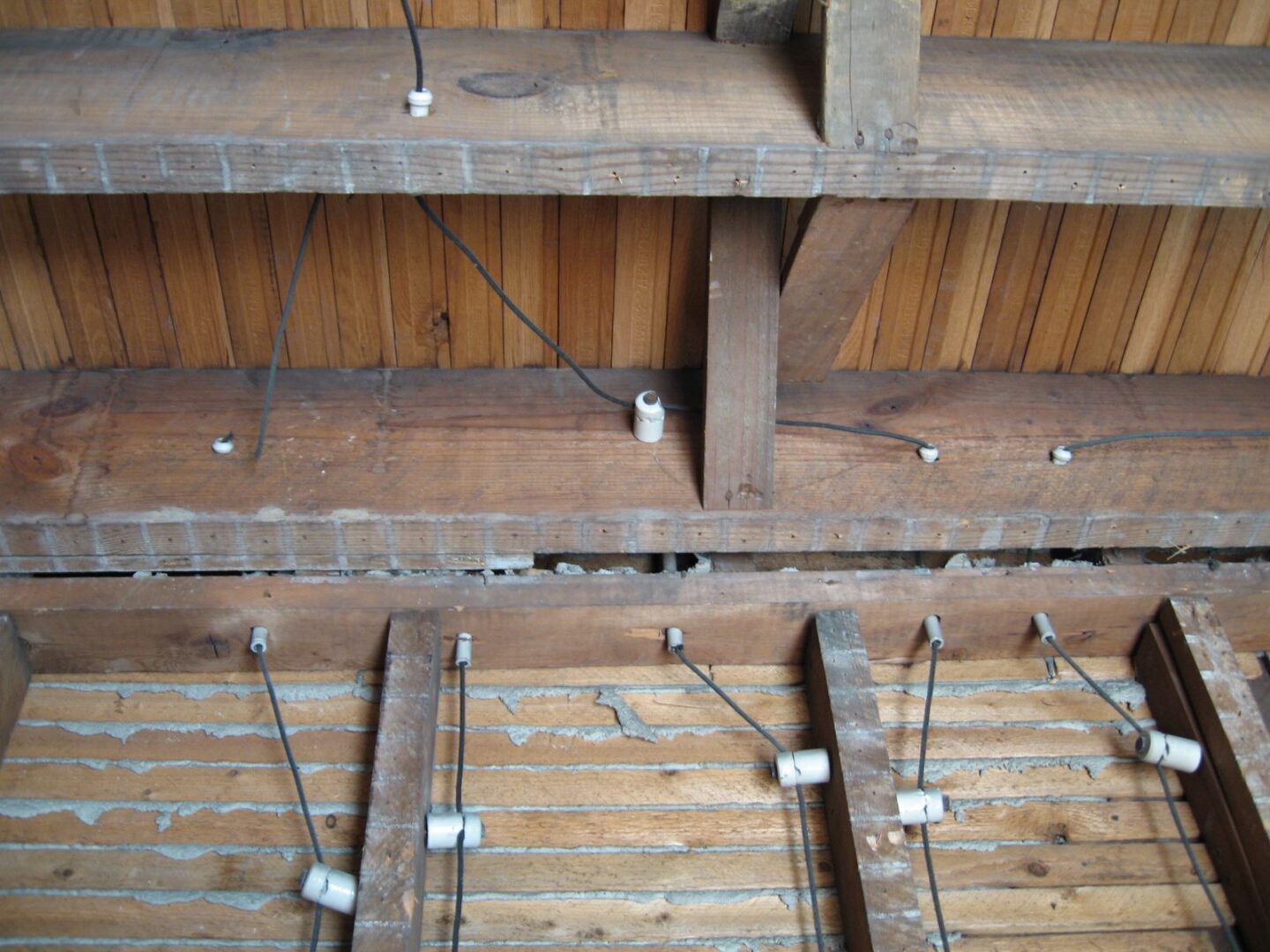 Knob and tube wiring strung on white ceramic knobs across the rafters and joists of a 1930s attic.