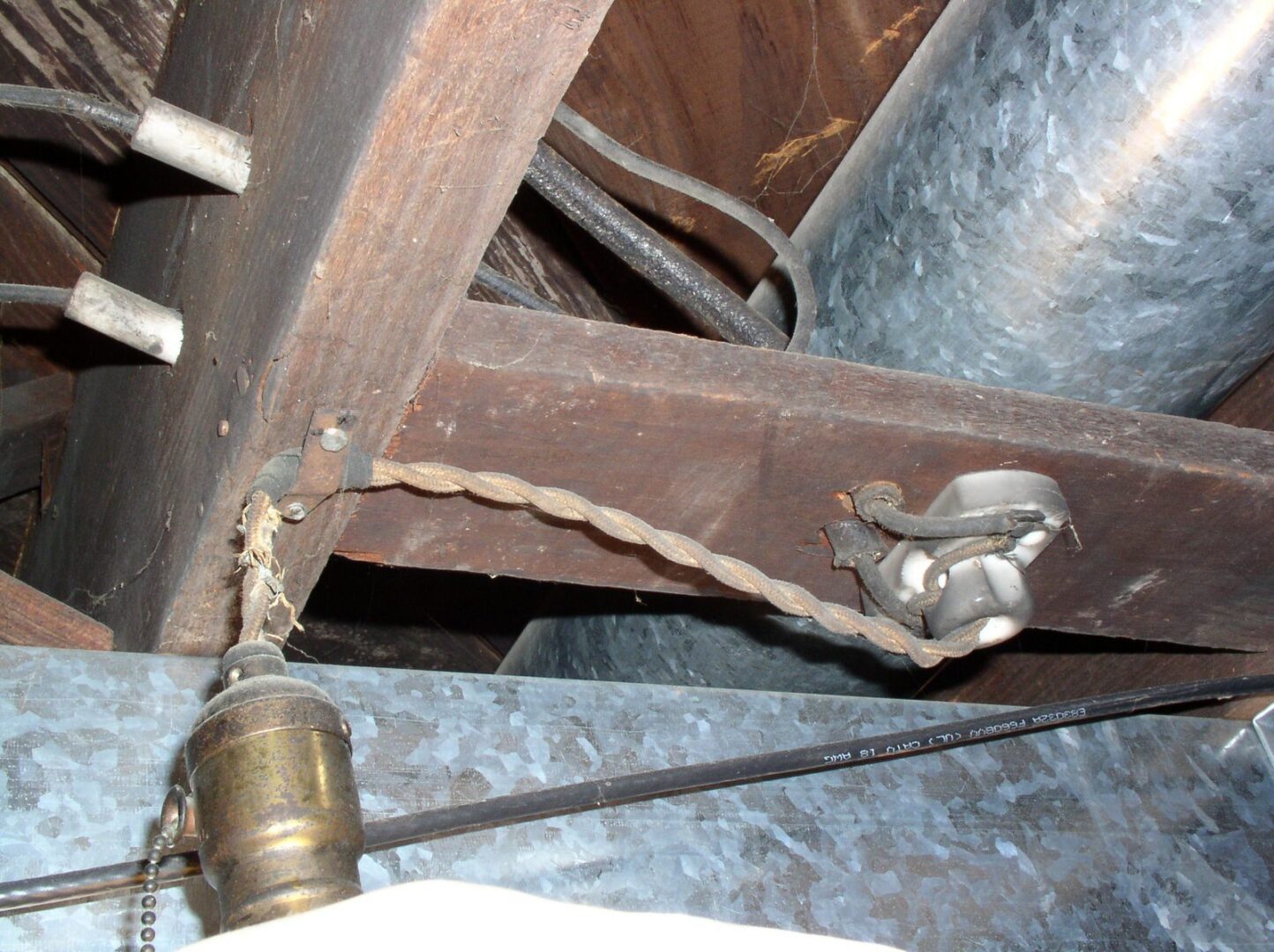 Old cloth covered wiring with a taped splice on a ceramic knob feeding a brass light socket beside galvanized ductwork.