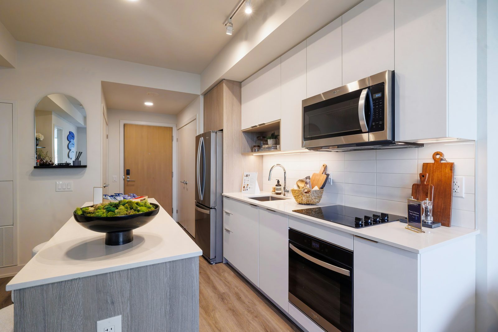 A modern white kitchen with a black glass cooktop, wall oven, stainless fridge and a gray island.