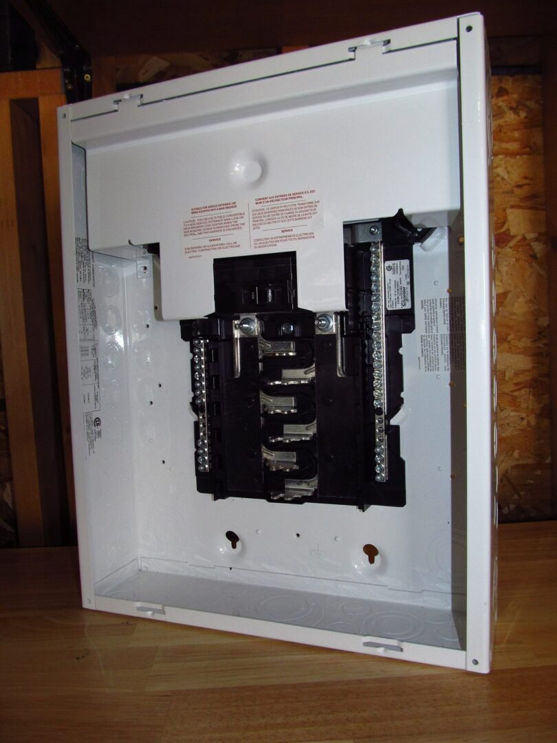 A brand new white residential load center with its cover off, bus bars and main breaker visible, leaning against a wall before installation.