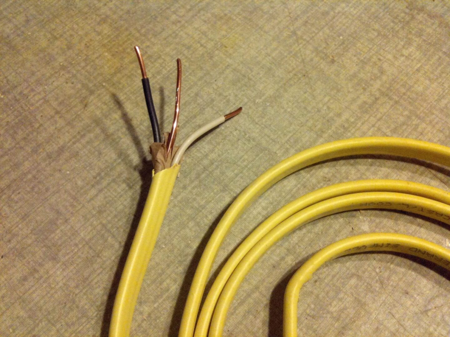 A coil of yellow 12 gauge NM cable with one end stripped to show the black, white and bare copper conductors.