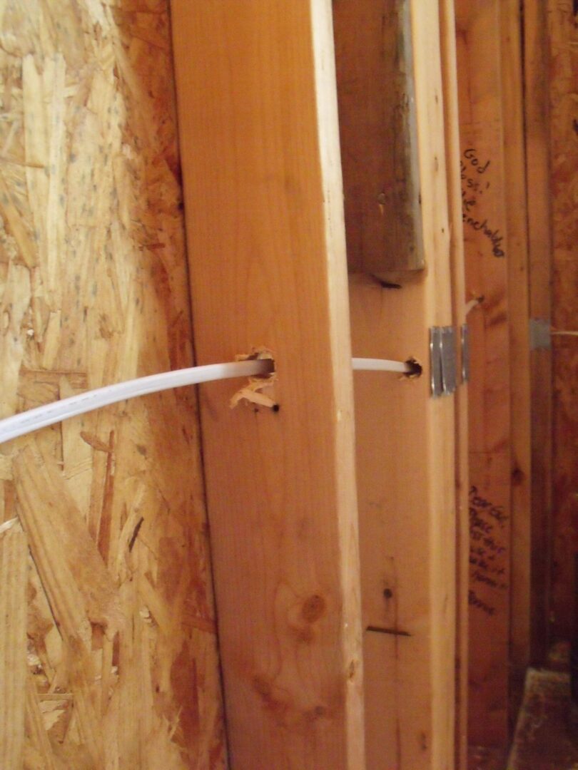 White NM cable running through drilled holes in wood studs with a nail plate during a rough in.