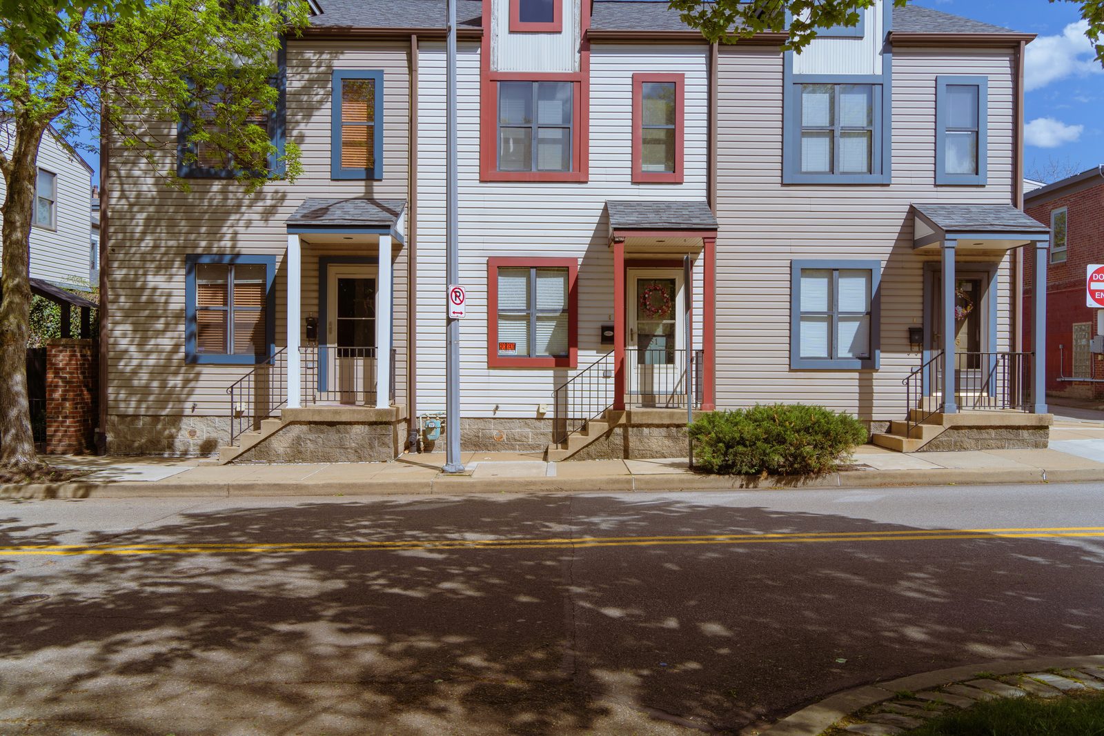 A row of attached two story houses with tan siding and red and blue trim on a quiet street.