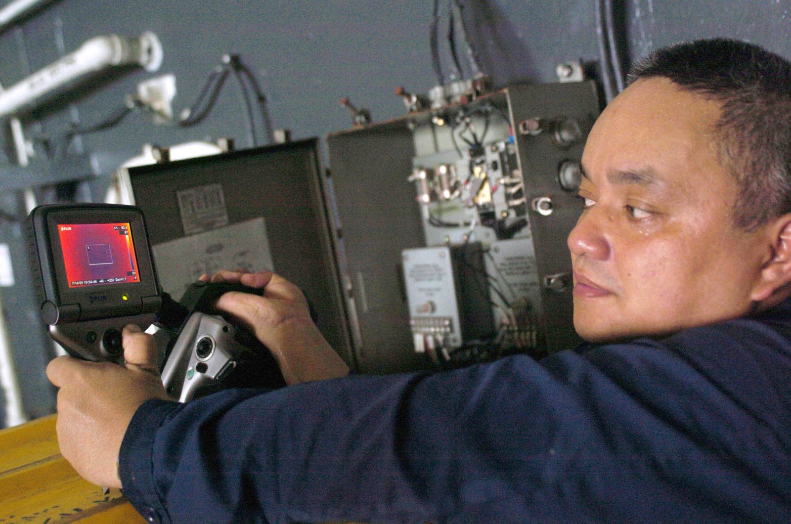 A technician aims a handheld thermal imaging camera at electrical equipment to check for hot spots.