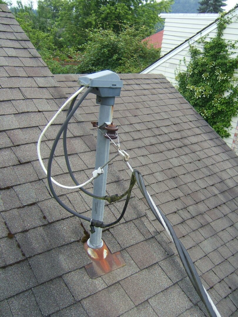 Close up of a gray service mast and weatherhead on an asphalt shingle roof with the triplex service drop looped into it.
