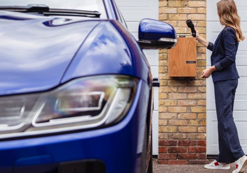 Woman charging an electric car at a home EV station, promoting charger rebates and incentives